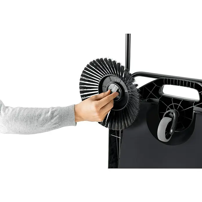 Kärcher Handkehrmaschine S 4 Twin Go!Further - Flächenleistung: 2.400 m²/h, 20 l - Hand justiert eine schwarze rotierende Bürste an einer schwarzen Kehrmaschine mit grauem Rad. Die Bürste zeigt Borsten und Mechanismus.
