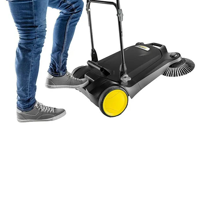 Kärcher Handkehrmaschine S 4 Twin Go!Further - Flächenleistung: 2.400 m²/h, 20 l - Person bedient eine schwarze Kärcher Kehrmaschine mit gelben Rädern, trägt Jeans und graue Turnschuhe.