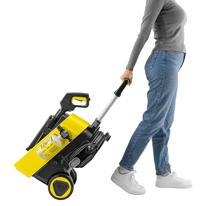 Kärcher Hochdruckreiniger K 7 Comfort Premium - 180 bar, 3.000 W, Fördermenge: 600 l/h, Ohne Home-Kit - Eine Person in Jeans und grauem Shirt zieht einen gelb-schwarzen Hochdruckreiniger mit ausziehbarem Griff auf Rädern.