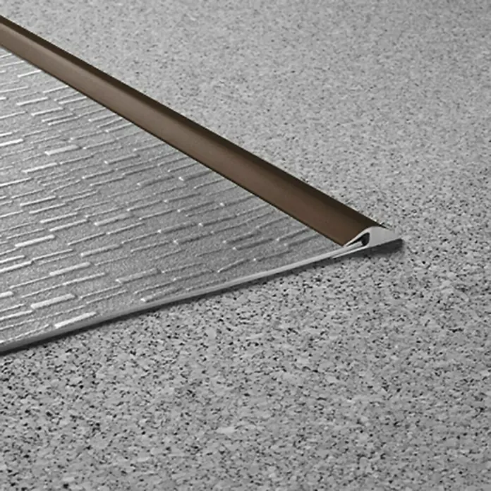 LOGOCLIC Einfassleiste - Braun, 1 m x 26 mm x 3 mm, Montageart: Kleben - Bild eines Bodenprofils mit brauner Kante, das den Übergang zwischen einem strukturierten Belag und einem gesprenkelten Bodenbelag bildet.