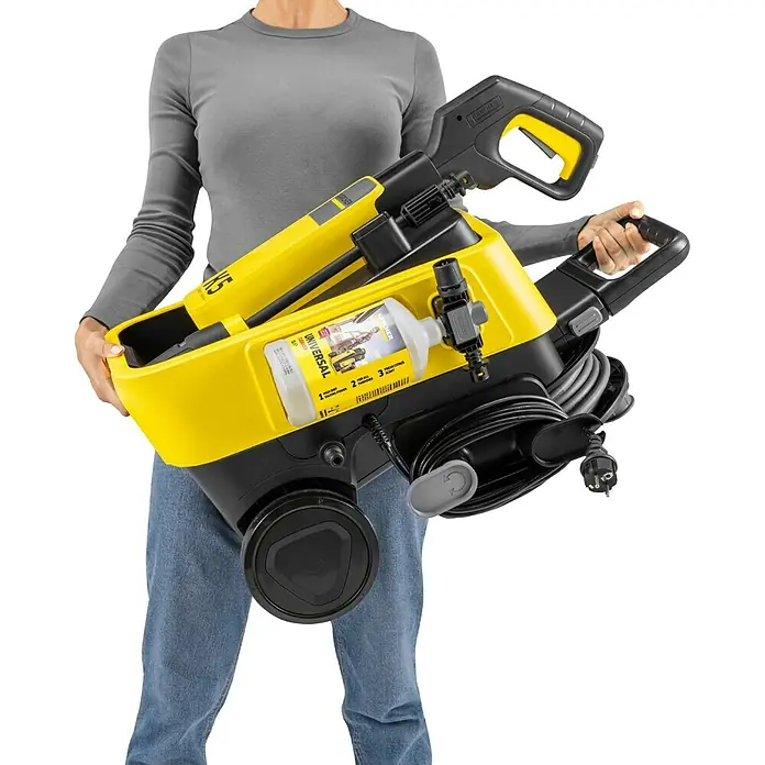 Kärcher Hochdruckreiniger K 5 Comfort Premium - 145 bar, 2.100 W, Fördermenge: 500 l/h, Ohne Home-Kit - Eine Person hält einen gelb-schwarzen Kärcher Hochdruckreiniger mit Reinigerflasche.