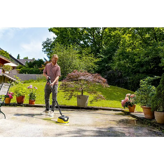 Kärcher Hochdruckreiniger K 4 Comfort Premium Home - 120 bar, 1.800 W, Fördermenge: 420 l/h, Inkl. Home-Kit - Ein Mann nutzt einen gelb-schwarzen Hochdruckreiniger-Flächenreiniger zur Terrassenreinigung.