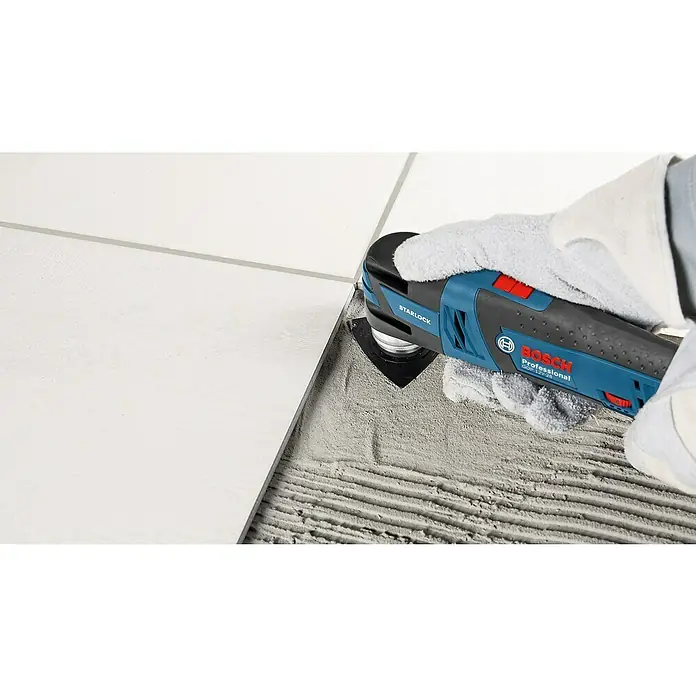 Bosch Professional Maschinen-Set 5-Tool-Kit GSR+GOP+GHO+GWS+GST - 12 V, 3 Akkus, 2 Ah - 3 Ah, 10 -tlg. - Blau-schwarzes Bosch Professional GOP 12V-28 Multifunktionswerkzeug, von behandschuhter Hand gehalten, schneidet Fugen zwischen weißen Fliesen.