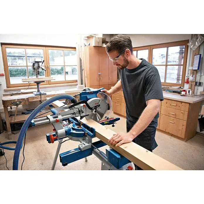 Bosch Professional Kapp- & Gehrungssäge GCM 305-254 D - 1.500 W, Durchmesser Sägeblatt: 254 mm, Leerlaufdrehzahl: 4.500 U/min - Blaue und silberne Kapp- und Gehrungssäge, bedient von einem Mann, der ein Holzbrett in einer Werkstatt sägt.