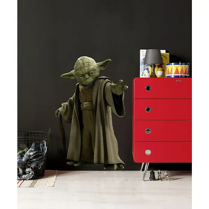 Komar Star Wars Wandtattoo Yoda - 70 x 100 cm - Yoda-Figur, die neben einer roten Kommode mit Zubehör und einer schwarzen Wäschetruhe steht, ideal für Star Wars-Fans.
