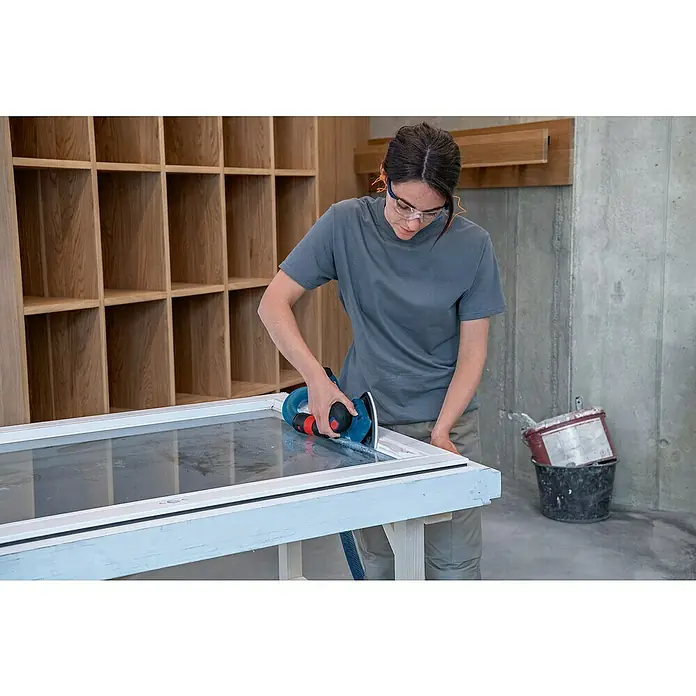Bosch Professional Akku-Schwingschleifer GSS 12V-13 PRO SOL - Ohne Akku, Leerlaufschwingzahl: 12.000 U/min - 20.000 U/min, 12 V - Eine Person schleift einen weißen Fensterrahmen mit einem blau-schwarzen Exzenterschleifer.