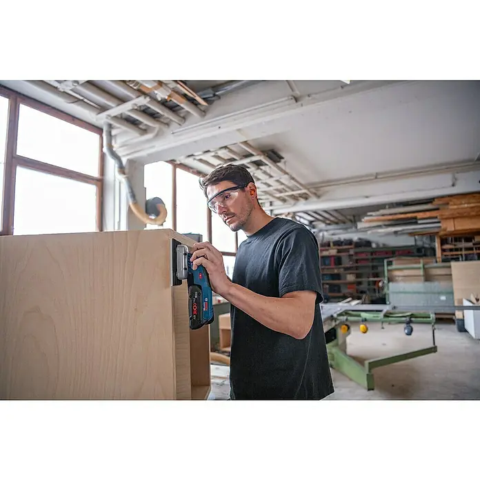 Bosch Professional AMPShare 18V Akku-Schwingschleifer GSS 18V-13 - Anzahl Akkus: Ohne Akku, Leerlaufschwingzahl: 12.000 U/min - 20.000 U/min, 18 V - Mann schleift in Werkstatt einen Holzschrank mit blau-schwarzem Bosch Akku-Schleifer, trägt Schutzbrille.