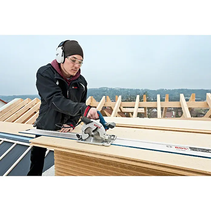 Bosch Professional Handkreissäge GKS 55+ GCE - 1.350 W, Durchmesser Sägeblatt: 165 mm - Person nutzt silber-blaue Bosch Handkreissäge mit Führungsschiene, um eine große Holzplatte auf dem Dach zu schneiden.