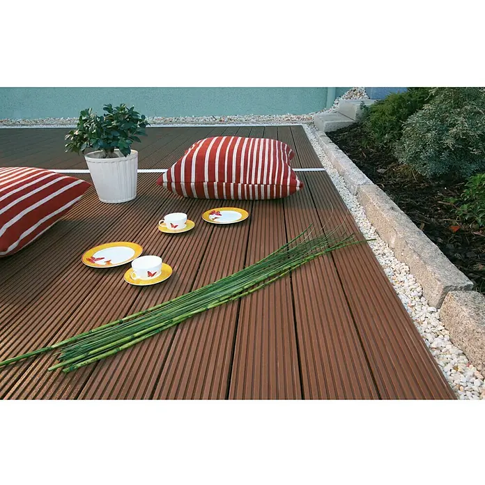 Kovalex WPC-Terrassenpaket Exklusiv - Braun, 4 x 4,95 m - Terrassendielen aus Holzverbundstoff mit Kissen, Geschirr und grünen Stängeln, die ein gemütliches Outdoor-Ambiente schaffen.