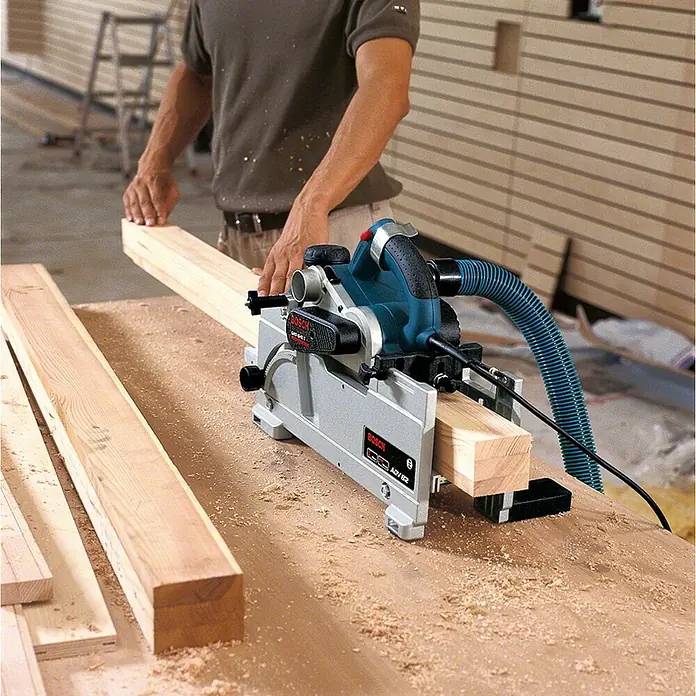 Bosch Professional Elektrohobel GHO 40-82 C - Hobeltiefe: 4 mm, Leerlaufdrehzahl: 14.000 U/min - Eine Person schneidet einen Holzbalken mit einer blauen und grauen Bosch Tauchsäge, an eine Absaugung angeschlossen, auf sägemehlbedecktem Tisch.