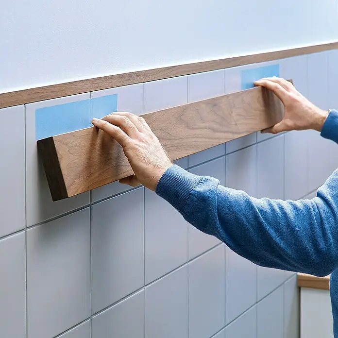 Tesa Montageband - Geeignet für: Fliesen, Belastbarkeit pro m: 100 kg, 1,5 m x 19 mm - Die Installation einer Holzleiste an einer gefliesten Wand mit blauem Klebeband zeigt ein DIY-Heimwerkerprojekt. Das Holz verleiht dem Raum Wärme.