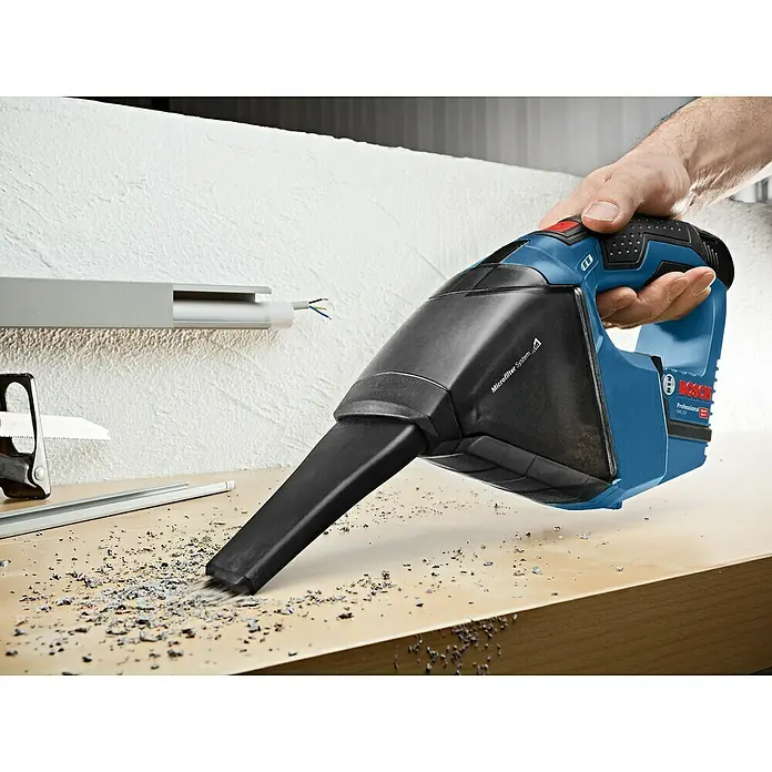 Bosch Professional Akku-Staubsauger - 12 V, 2 Akkus, Behältervolumen: 0,35 l - Eine Person reinigt mit einem blau-schwarzen Bosch Handstaubsauger Holzspäne von einer Werkbank.