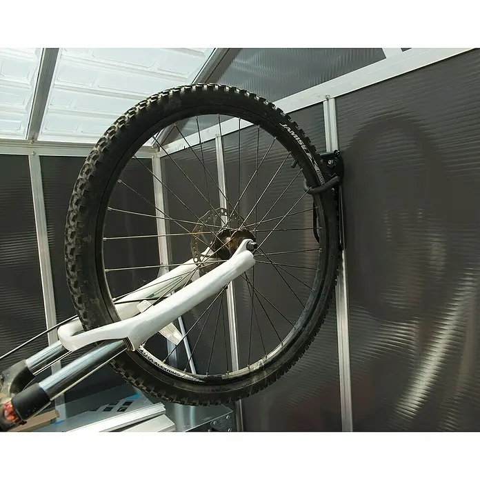 Palram – Canopia Fahrrad-Wandhaken - Passend für: Mountainbikes mit Laufrädern von 36 bis 74 cm (14" bis 29") - Ein Fahrradvorderrad mit schwarzem Reifen und weißer Federgabel, vertikal an einer dunkelgrauen gerippten Wand mit schwarzem Haken montiert.