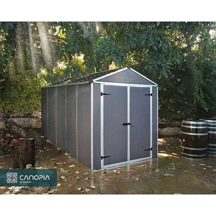 Palram – Canopia Gartenhaus Rubicon - Außenmaß inkl. Dachüberstand (B x T): 1,85 x 3,78 m, Kunststoff, Grau - Dunkelgraues Gartenhaus mit silbernen Akzenten, das in einem Garten mit Wasser besprüht wird, was seine Wetterbeständigkeit zeigt.