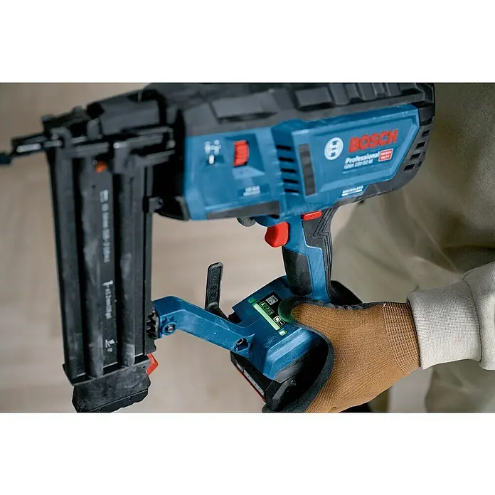 Bosch Professional Akku-Nagler GNH 18V-50 M PRO SOLO - 18 V, Ohne Akku, Länge Nagel: 16 mm - 50 mm - Eine Person mit braunem Handschuh hält eine blau-schwarze Bosch Akku-Nagelpistole. Batteriestatusleuchten sind sichtbar.