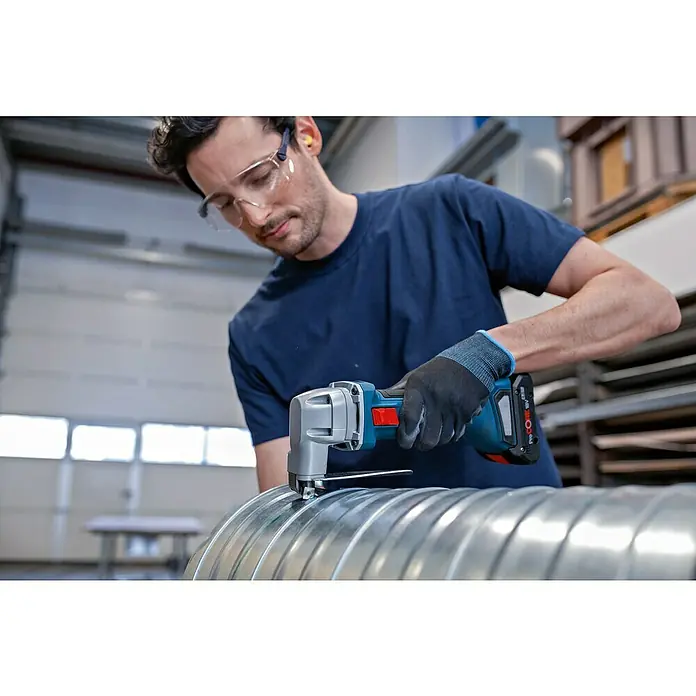 Bosch Professional AMPShare 18V Akku-Blechschere Heavy Duty GSC 18V-16 E - 18 V, Ohne Akku, Leerlaufhubzahl: 3.200 /min - Mann in Schutzausrüstung schneidet ein gewelltes Metallrohr mit einer blau-grauen Akku-Blechschere.