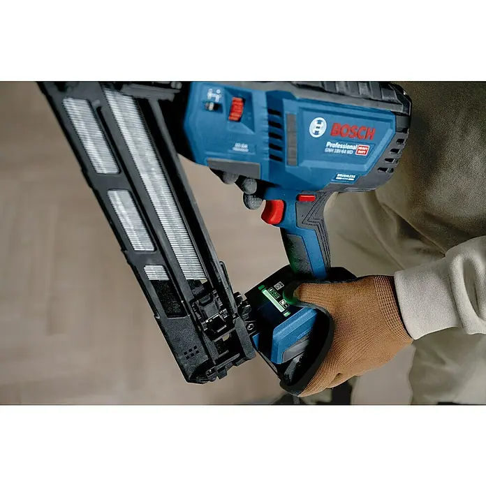 Bosch Professional Elektronagler GNH 18V-64 MD PRO SOLO - Länge Nagel: 32 mm - 64 mm, Magazinkapazität Nägel: 105 Stk. - Blauer Bosch Akku-Nagler, von einer behandschuhten Hand gehalten. Das schwarze Magazin ist voll Nägel, grüne Lichter zeigen den Akkuladestand.
