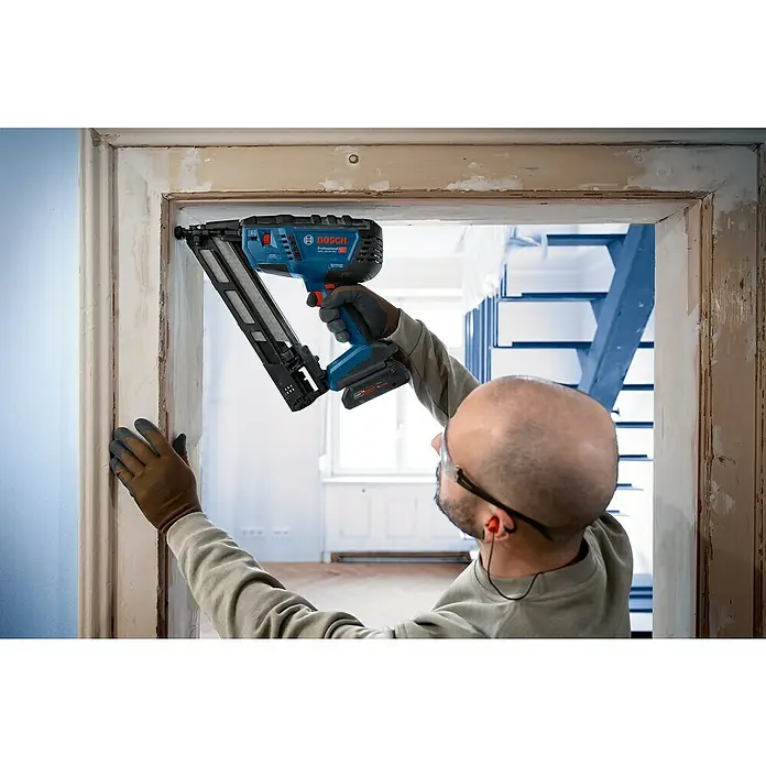 Bosch Professional Elektronagler GNH 18V-64 MD PRO SOLO - Länge Nagel: 32 mm - 64 mm, Magazinkapazität Nägel: 105 Stk. - Blauer und schwarzer Bosch Profi-Nagler, der von einer Person zum Befestigen von Holzleisten an einem Türrahmen verwendet wird.