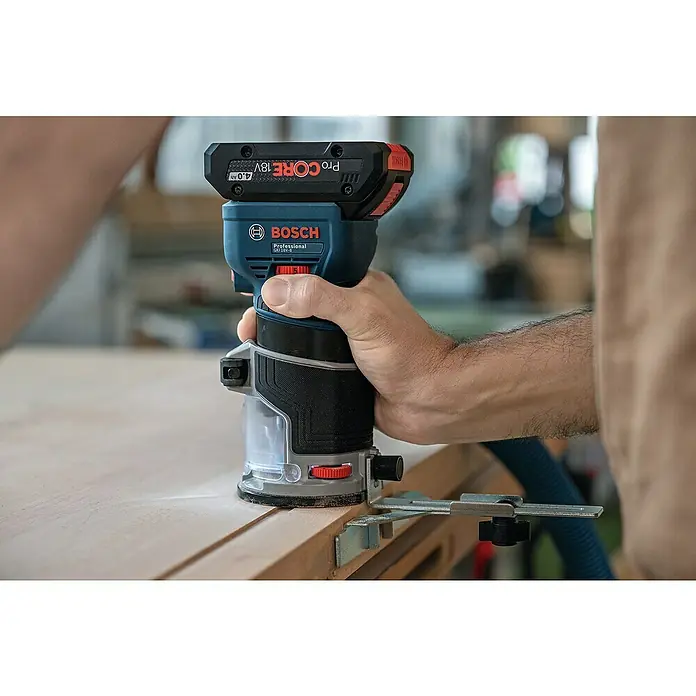 Bosch Professional AMPShare 18V Akku-Kantenfräser GKF 18V-8 PRO SOLO - 18 V, Ohne Akku, Leerlaufdrehzahl: 10.000 U/min - 30.000 U/min - Eine Hand hält einen blauen und schwarzen Bosch Professional Akku-Oberfräser mit rotem 18V Akku, der die Kante eines Holzbretts mit Führung fräst.