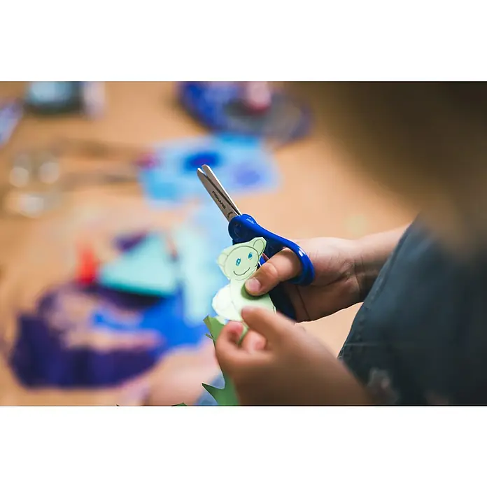 Fiskars Bastelschere - Länge: 131 mm, Blau - Kinderhände halten blaue Schere, schneiden grünen Papierbären.