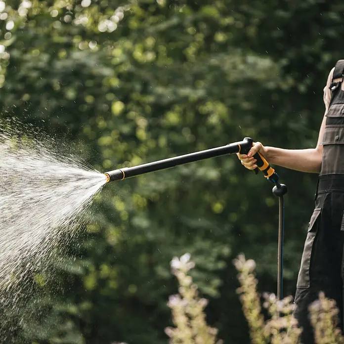 Fiskars Gießstab Comfort - Länge: 76 cm, Aluminium - Person hält eine schwarz-gelbe Gießbrause und besprüht einen Garten mit Wasser.