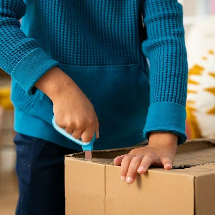 Fiskars Bastel-Set Kreativset für Kinder aus Pappe - 2 -tlg. - Kinderhände öffnen mit blauem Sicherheitsmesser einen Karton.