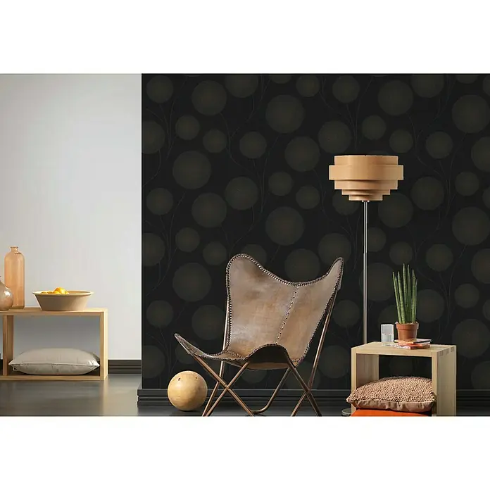 A.S. Création Vliestapete Blütenmuster - Schwarz/Metallic, Floral, 10,05 x 0,53 m - Brauner Ledersessel mit kupferfarbenem Rahmen vor einer Wand mit einem Kreismuster. Der Sessel ist das zentrale Element des Bildes.
