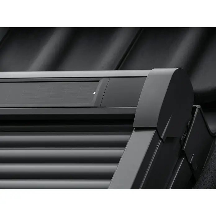Velux Dachfenster-Rollladen Solar SSL CK06 0000K - Passend für Fenstergröße: CK06, C06, Passend für Fenstertyp: GGL, GGU, GPL, GPU, GHL, GHU, GZL, GLL, GLU, VU und VKU - Nahaufnahme eines dunkelgrauen, solarbetriebenen Rollladens mit horizontalen Lamellen und integriertem Solarpanel auf einem Dach.