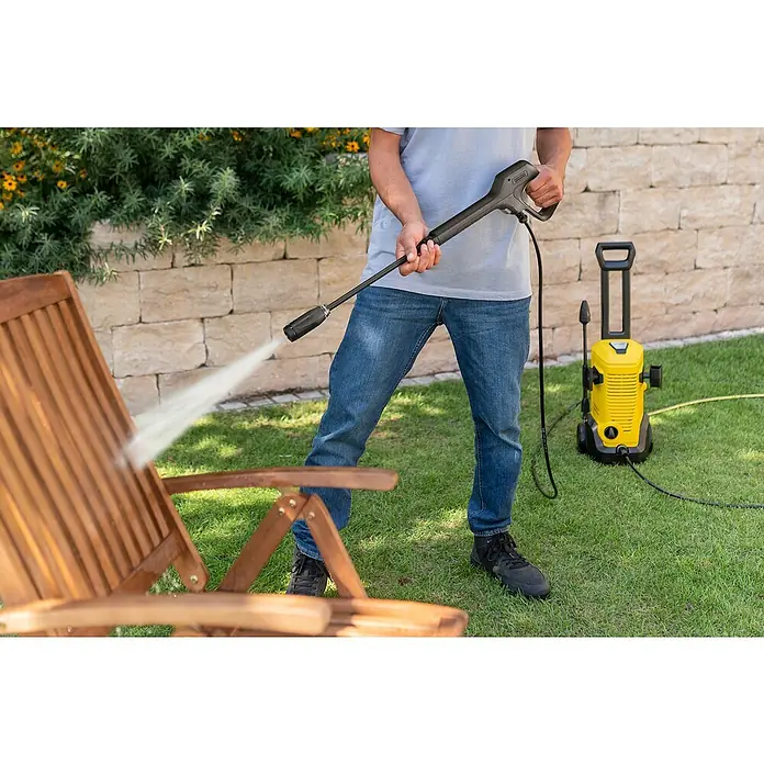 Kärcher Strahlrohr VP 135 Vario Power Jet - Passend für: Kärcher Hochdruckreiniger K 2 bis K 3 - Person reinigt einen Holzstuhl im Freien mit einem gelb-schwarzen Kärcher Hochdruckreiniger.