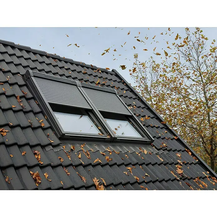 Velux Dachfenster-Rollladen Solar SSL CK06 0000K - Passend für Fenstergröße: CK06, C06, Passend für Fenstertyp: GGL, GGU, GPL, GPU, GHL, GHU, GZL, GLL, GLU, VU und VKU - Dunkelgraues Dachfenster mit geschlossenem Rollladen, in ein Ziegeldach im Herbst integriert.