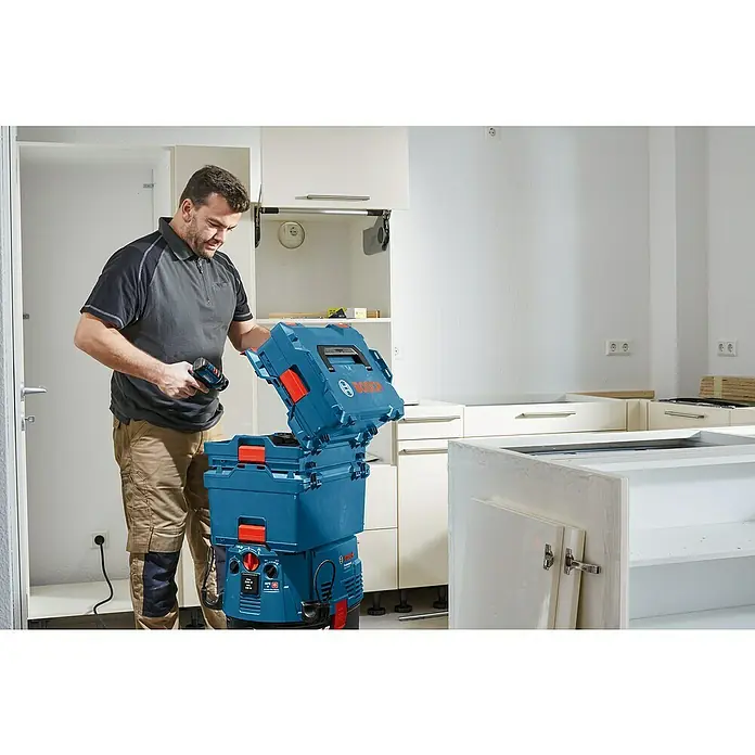 Bosch Professional Werkzeugkasten I-BOXX Rack Active Pro - ABS, Passend für: I-Boxx, L-Boxx, LS Tray - Mann installiert Küche, hält Bosch-Bohrmaschine und öffnet blauen Bosch L-Boxx Werkzeugkoffer auf einem Bosch Staubsauger.
