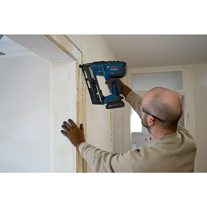 Bosch Professional Akku-Nagler GNH 18V-64-2 M PRO SOLO - 18 V, Ohne Akku, Länge Nagel: 32 mm - 64 mm - Mann benutzt ein blau-schwarzes Bosch Profi-Nagelgerät an einem Türrahmen.