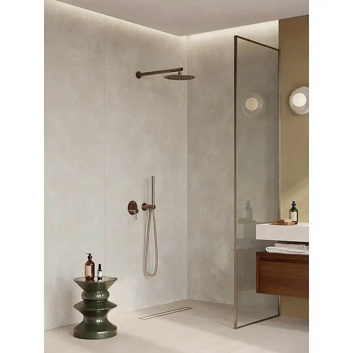 Corso Italia Feinsteinzeugfliese Resin - 120 x 278 cm, Silber, Matt - Moderner Duschbereich mit bronzefarbenen Regen- und Handbrausearmaturen auf hellgrauen Fliesen, inkl. dunkelgrünem Hocker und Linienablauf.