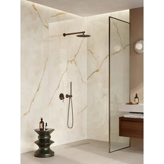 Corso Italia Feinsteinzeugfliese Onyx - 120 x 278 cm, Gold, Glänzend - Eine moderne Dusche mit hellen Onyx-Effekt Wandfliesen und einem bronze Regenduschkopf mit Handbrause.