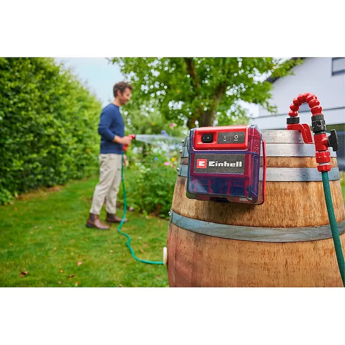 Einhell Power X-Change 18V Akku-Regenfasspumpe GE-PP 36 RB-A Li-Solo - Max. Fördermenge: 4.500 l/h - Rote und transparente Einhell Wasserpumpe an einer Regentonne, versorgt einen Schlauch zum Bewässern von Pflanzen im Garten.