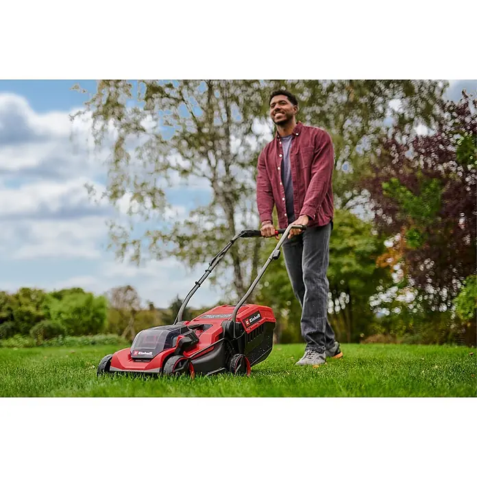 Einhell Power X-Change 18V Akku-Rasenmäher GE-CM 18/32 C Li BL - 18 V, Ohne Akku, Schnittbreite: 32 cm - Ein Mann mäht mit einem roten und schwarzen Akku-Rasenmäher Gras im Garten.