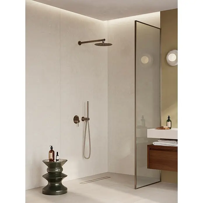 Corso Italia Feinsteinzeugfliese Resin - 120 x 278 cm, Weiß, Matt - Modernes Duschbad mit hellen Strukturwänden, bronzenen Armaturen und dunkelgrünem Hocker. Holzwaschtisch und Waschbecken hinter Glaswand.