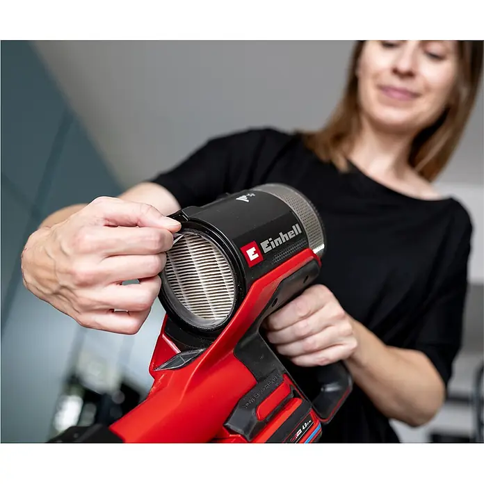 Einhell Staubfilter - Passend für: Einhell Akku-Stielstaubsauger TE-SV 18/270 Li BL-Solo und TE-SV 18/270 Li BL-C Solo - Hände entfernen oder prüfen den Filter eines rot-schwarzen Einhell Handstaubsaugers.