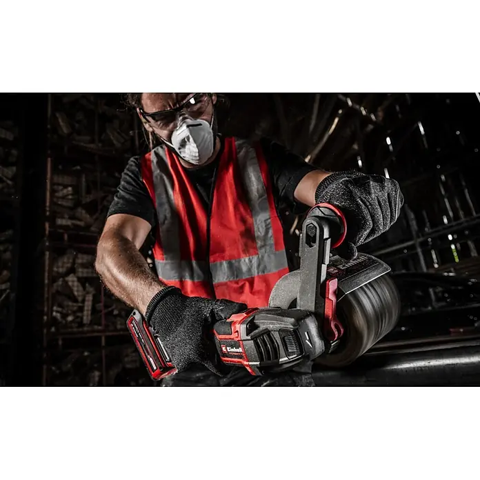 Einhell Messingdrahtbürste - Passend für: Einhell Akku-Bürstenschleifer TP-BR 18/32 Li BL - Rotes und schwarzes Einhell Akku-Elektrowerkzeug, von einem Arbeiter mit Schutzkleidung gehalten, bearbeitet eine Metalloberfläche. Akku sichtbar.
