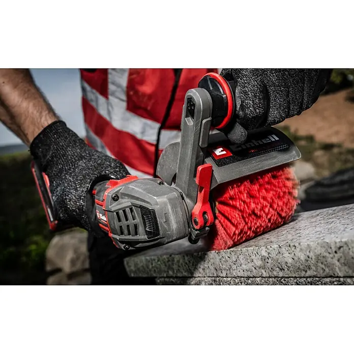 Einhell Bürstenwalze - Passend für: Einhell Akku-Bürstenschleifer TP-BR 18/32 Li BL, Geeignet für: Holz/Metall - Person benutzt rotes und graues Akku-Elektrowerkzeug mit rotem Bürstenkopf auf grauem Stein.