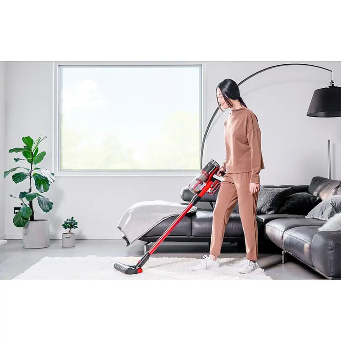 Einhell Power X-Change 18V Akku-Staubsauger TE-SV 18/270 Li BL-Solo - 18 V, Ohne Akku, Behältervolumen: 0,85 l - Frau reinigt einen weißen Teppich im modernen Wohnzimmer mit einem roten und schwarzen Akku-Stielstaubsauger.