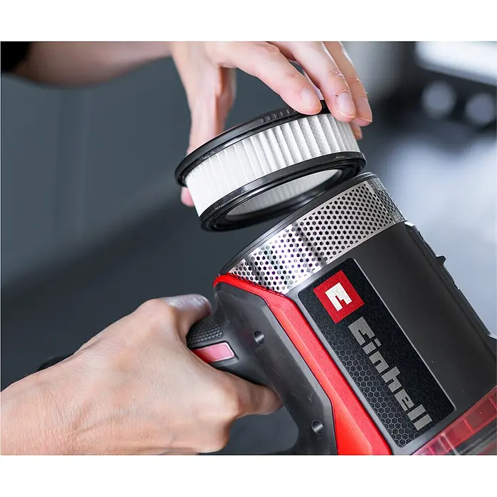 Einhell Filter - Passend für: Einhell Akku-Stielstaubsauger TE-SV 18/270 Li BL-Solo und TE-SV 18/270 Li BL-C Solo - Hände setzen einen weißen Filter in einen schwarz-roten Einhell Handstaubsauger ein.