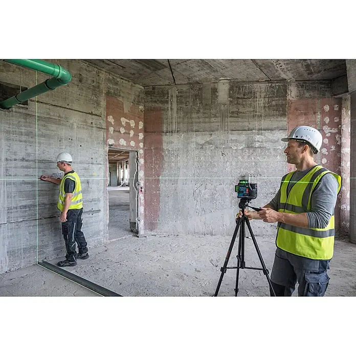 Bosch Professional Linienlaser GLL 12V-100-33 CG PRO - Max. Arbeitsbereich: 30 m - Ein blau-schwarzer Bosch Linienlaser auf einem Stativ projiziert grüne Linien auf Betonwände, geleitet von Bauarbeitern.
