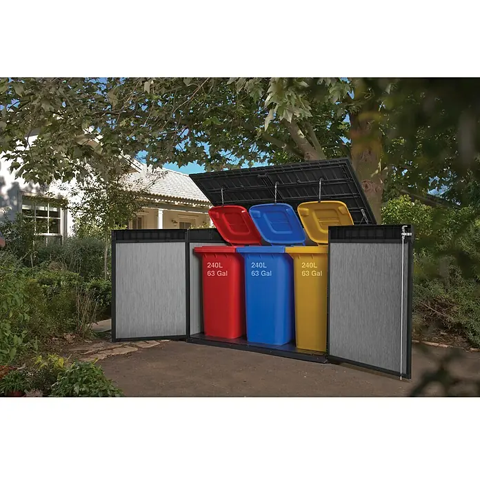 Keter Truhe Grande Store - Außenmaß inkl. Dachüberstand (B x T): 191 x 109 cm, Kunststoff, Grau, Geeignet für Anzahl Mülltonnen: 3 Stk. - Das Bild zeigt eine Mülltonnenbox mit drei farbigen Mülltonnen (Rot, Blau, Gelb) in einem Garten mit einem Haus im Hintergrund.