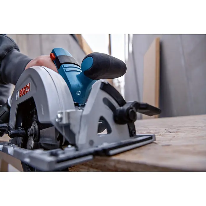 Bosch Professional Akku-Handkreissäge - 18 V, 2 Akkus, Durchmesser Sägeblatt: 165 mm, 5.000 U/min - Eine blau-graue Bosch Handkreissäge, von einer Person gehalten, auf einem Holzbrett liegend, bereit zum Sägen.