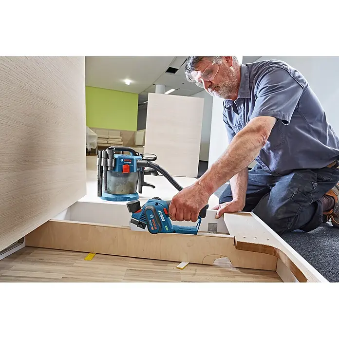 Bosch Professional Akku-Hobel GHO 12V-20 PRO - 12 V, 2 Akkus, Hobeltiefe: 0 mm - 2 mm, Leerlaufdrehzahl: 14.500 U/min - Mann nutzt Bosch Professional Akku-Hobel und Staubsauger zum Glätten von Holz.