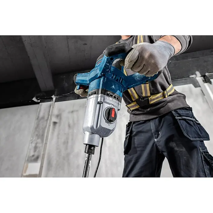 Bosch Professional Rührwerk GRW 140 - 1.400 W - Eine Person in Arbeitskleidung hält ein blau-silbernes Bosch Elektrowerkzeug, möglicherweise einen Mischer oder Bohrhammer, bereit zum Einsatz.