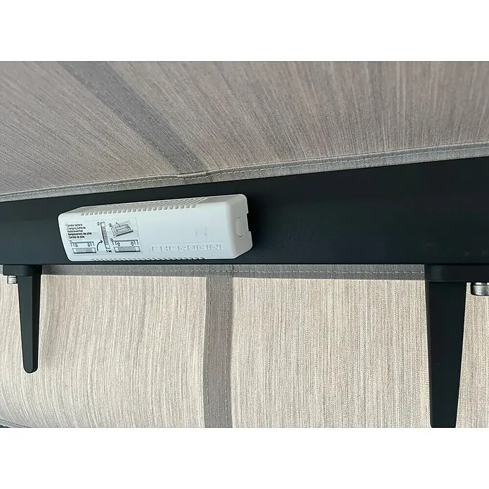 Spettmann Windsensor - 140 x 38 x 26 mm, Passend für: Spettmann offene Gelenkarm-, Halbkassetten- und Vollkassettenmarkisen - Weißes Cherubini Batteriefach mit mehrsprachigen Anweisungen zum Batteriewechsel, montiert auf einer schwarzen Stange über einem hellgrauen Stoffrollo.