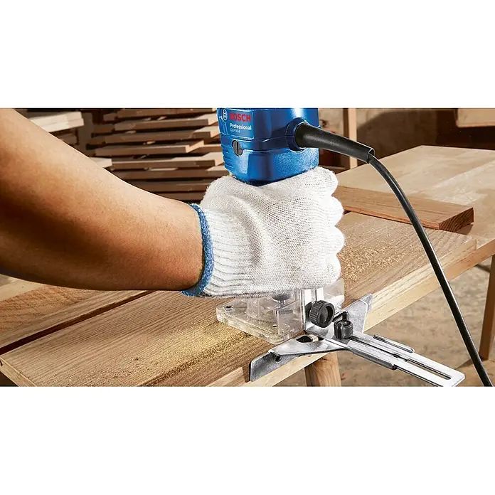 Bosch Professional Elektro-Oberfräse GLF 55-6 - 550 W, 33.000 U/min - Blauer Bosch-Fräser mit klarer Basis und Metallführung, von einer behandschuhten Hand auf Holz bedient, Sägespäne erzeugend.