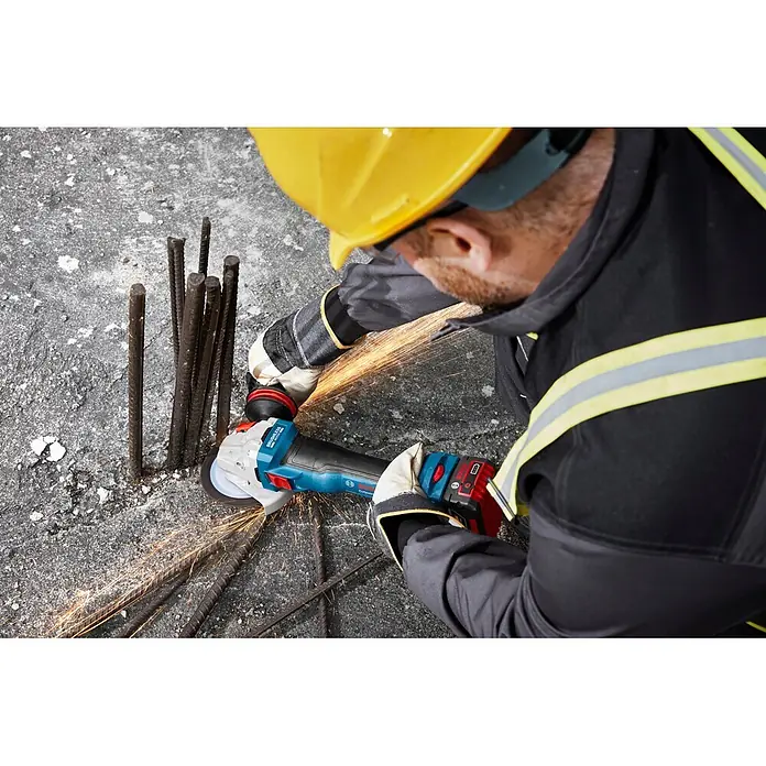 Bosch Professional AMPShare 18V Akku-Winkelschleifer GWS 18V-11 S PRO - Ohne Akku, Durchmesser Scheibe: 125 mm - Ein Arbeiter mit Helm und Handschuhen benutzt einen blau-schwarzen Akku-Winkelschleifer von Bosch, um Bewehrungsstahl zu schneiden, wobei Funken fliegen.